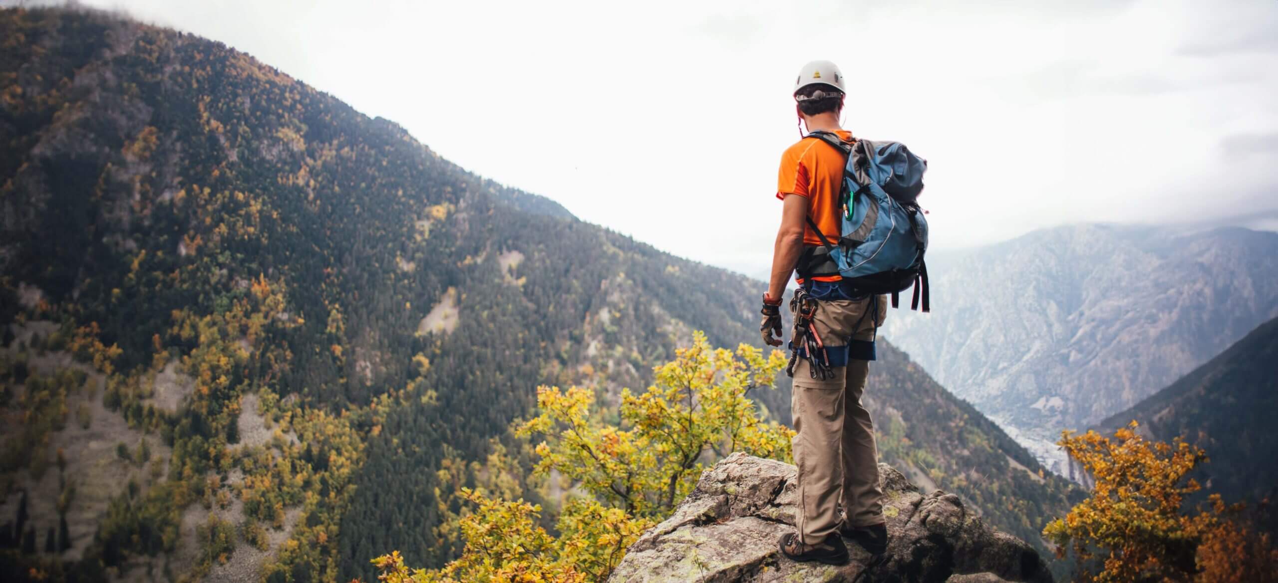 Hiker reaching the top point of his hike, looking over the view at mountains in the distance